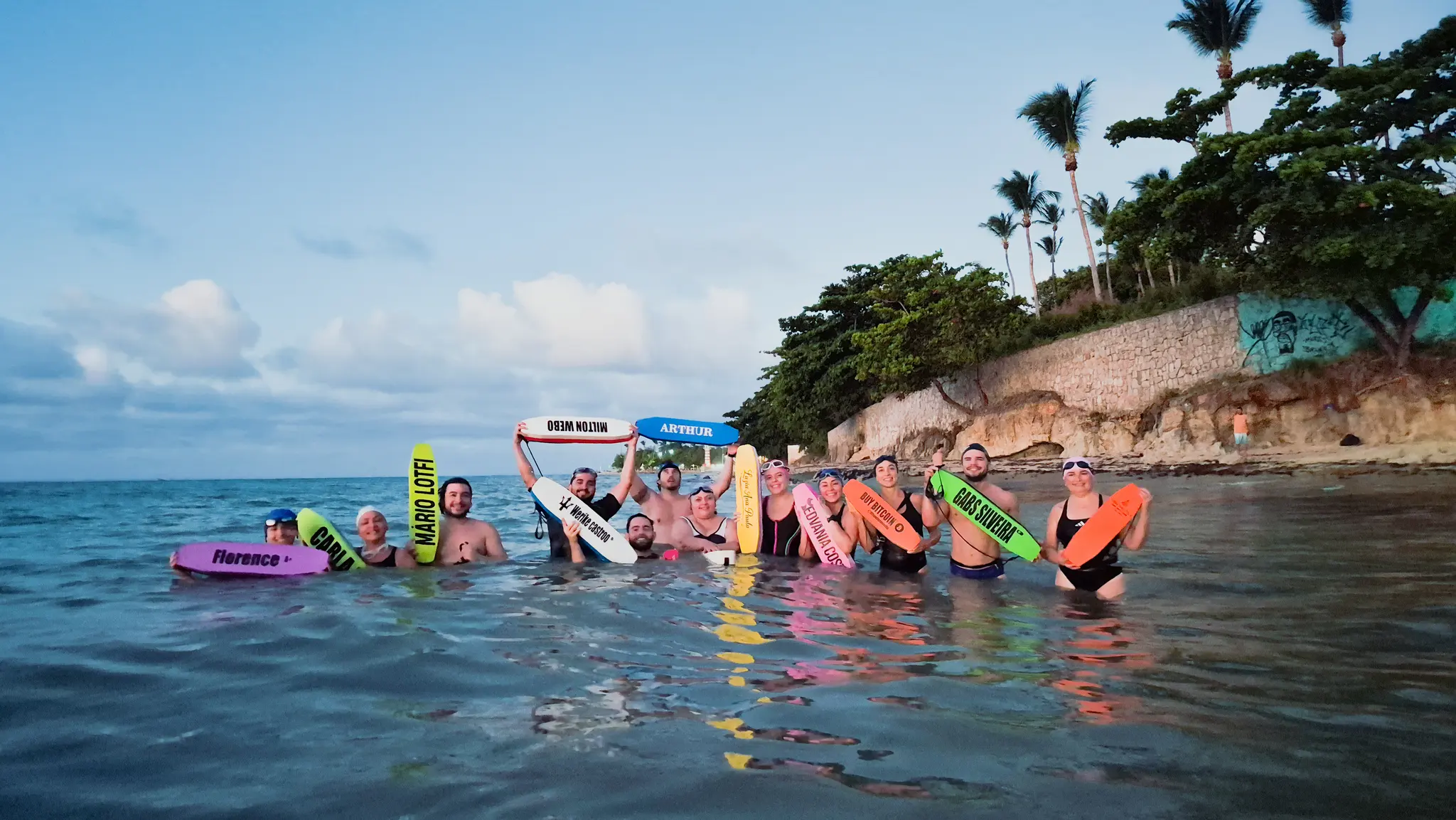 Equipe dentro do mar erguendo flutuadores coloridos, cada um com o nome do atleta